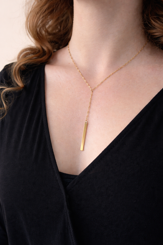 Vergoldete Y-Kette aus Edelstahl mit geradem Stabanhänger, minimalistisch am Dekolleté zu schwarzem Oberteil getragen