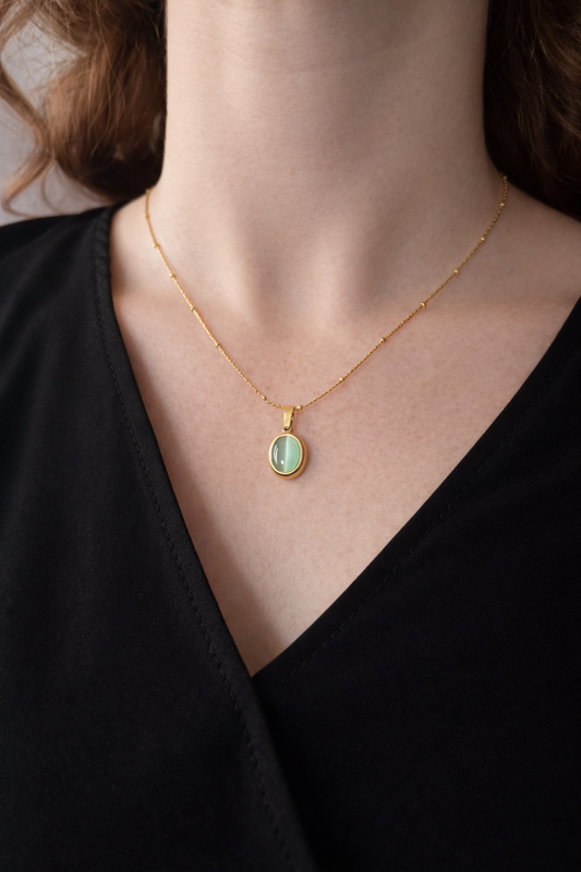 Vergoldete Kette aus Edelstahl mit ovalem Steinanhänger, elegant am Dekolleté zu schwarzem Oberteil getragen